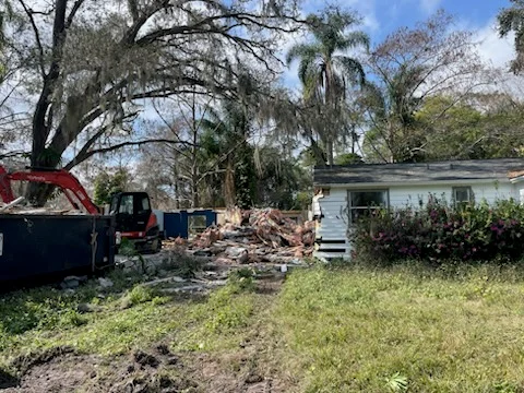 Red excavator and roll-off dumpster clearing debris from a demolished residential structure in Central Florida